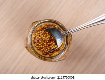 A Metal Spoon In A Jar Of Dijon Or French Mustard. Mustard Sauce With White Mustard And Black Mustard Seeds. Top View.