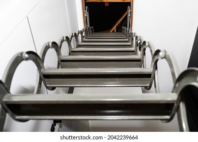 Metal Stairs Hidden In The Ceiling To The Attic With An Opening Hatch And Folding Stairs In The Corridor, View From The Bottom Of The Stairs Up, Modern Look.