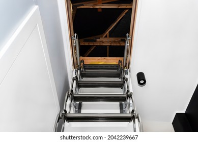 Metal Stairs Hidden In The Ceiling To The Attic With An Opening Hatch And Folding Stairs In The Corridor, View From The Bottom Of The Stairs Up, Modern Look.