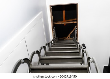 Metal Stairs Hidden In The Ceiling To The Attic With An Opening Hatch And Folding Stairs In The Corridor, View From The Bottom Of The Stairs Up, Modern Look.