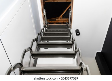 Metal Stairs Hidden In The Ceiling To The Attic With An Opening Hatch And Folding Stairs In The Corridor, View From The Bottom Of The Stairs Up, Modern Look.