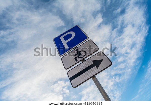 Metal support with road signs parking\
place, right signboard, sign of a place for the disabled against a\
blue sky with white clouds, abstract\
background