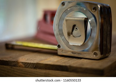 A Metal Tape Measure And Small Red Magnetic Spirit Level Sitting On Wood Table Background. DIY Home Repair, Decorating, Remodeling, And Home Improvement Equipment. Bubble Level. No People