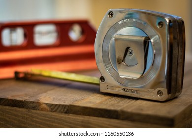 A Metal Tape Measure And Small Red Magnetic Spirit Level Sitting On Wood Table Background. DIY Home Repair, Decorating, Remodeling, And Home Improvement Equipment. Bubble Level. No People