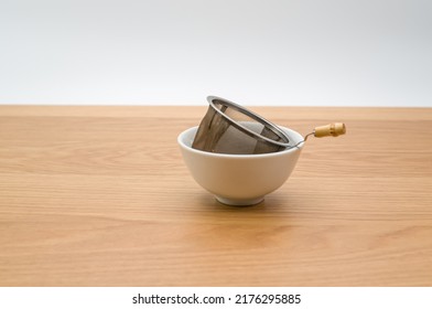 metal tea strainer with tea leaves in a ceramic bowl on a wooden background with text space