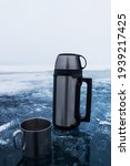 Metal thermos with a hot drink on the background of pure ice at Lake Baikal. Thermos for tea on a fishing trip.