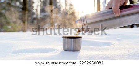 Metal thermos with a hot drink on the background of a winter mountain waterfall. Insulated drink container in the