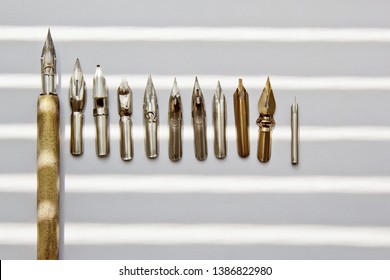 Metal Tips For The Ink Pen On A White Background In Solar Rays. Stationery On White Desk Close Up Top View. Spelling Lessons And Caligraphy Exercises. Template, Layout, Background. Macro.