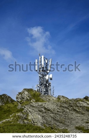 Metal tower with various telecommunication antennas on top of a mountain, against a background of blue sky, in early spring. Ensuring the operation of cellular communications in hard-to-reach places.