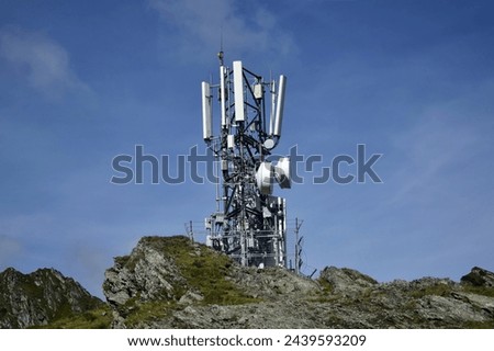 Metal tower with various telecommunication antennas on top of a mountain, against a background of blue sky, in early spring. Ensuring the operation of cellular communications in hard-to-reach places.