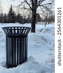 A metal trash can in a winter park, buried in snow