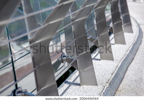 metal turnbuckles\
fastening of cables with steel rod on pedestrian bridge with stone\
pebble path and glass barrier for safety close-up details of\
construction, nobody.