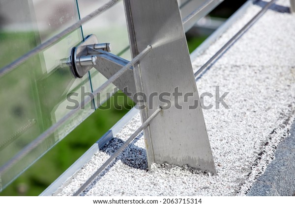 metal
turnbuckles fastening of cables with steel rod on pedestrian bridge
with stone pebble path and glass barrier for safety close-up
details of construction on sunny day,
nobody.