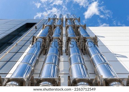 Metal ventilation pipes on the outer wall of a black and white industrial building against a blue sky background. Gas heating turbo boiler. bottom-up view.