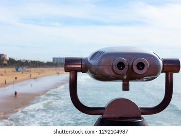 Metal Viewfinder Overlooking A Beach With The Ocean In The Background, Bright Blue Cloudy Sky.