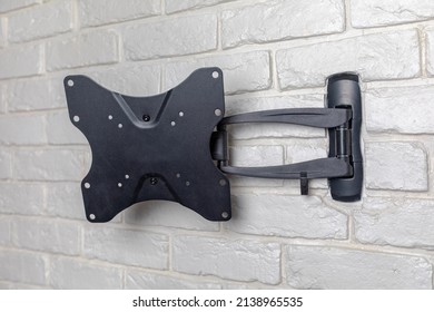 Metal Wall-mounted Black TV Bracket Hanging On The Wall Against A Background Of White Decorative Bricks.