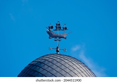 Metal weathervane in the form of a ship on the dome of the building against the blue sky