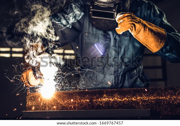 Metal welder working with arc welding machine to\
weld steel at factory while wearing safety equipment. Metalwork\
manufacturing and construction maintenance service by manual skill\
labor concept.