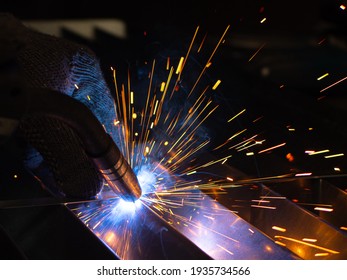 Metal welder works with a steel welder in a factory with protective equipment. Manufacture of metal structures and repair and construction services according to the concept of manual labor. - Shutterstock ID 1935734566