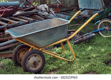 Metal Wheel Cart Parked On Grassy Lawn Near Pile Of Shabby Waste On Summer Day In Countryside Yard