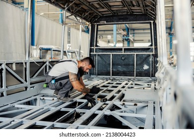 A metal worker crouching in skeleton of a new bus and building it at workshop.