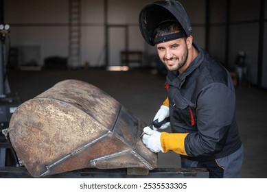 Metal worker wearing protective gear is using a plasma cutter on a large metal structure in a workshop - Powered by Shutterstock