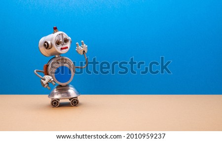 Metallic chat bot robot on blue beige background. Silver color domestic robotic roller with empty blue interface on body. Creative design steampunk toy, copy space.