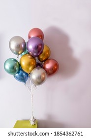 metallic coloured helium balloons tied with a bow and held by a weight on a green table, vertical format and copy space on the right