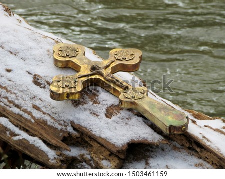 Metallic cross on log with winter snow and water background.