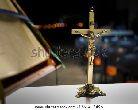 metallic cross placed on an altar before a catholic mass at night with blurred background and a liturgy book blurred on the foreground
