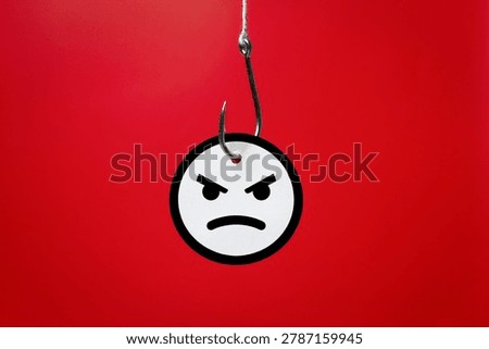 A metallic fishhook piercing an angry face emoji on a red background. Rage bait, social media trolling, online manipulation, clickbait traps, and deliberate digital provocation designed to drive user engagement concept.
