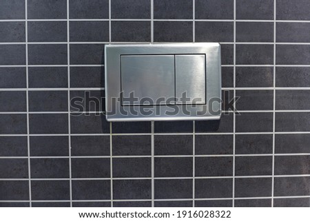 Metallic flush push button on wall in toilet