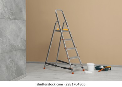 Metallic folding ladder and painting tools near beige wall indoors