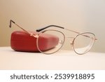 Metallic glasses with a black frame are leaning against a red elegant eyeglass case.