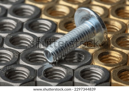 Metallic hex nuts and a fastener bolt with rivet, industrial background. Mix of steel and brass nuts
