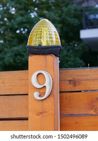 Metallic house number 9, nine and a signal lamp with flashing light on a wooden fence post