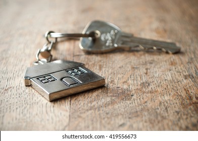 Metallic Key With House Shaped Key Chain On Wooden Background
