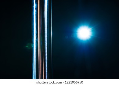 Metallic pole closeup and blue light from flash on dark background. Pole dance theme.
