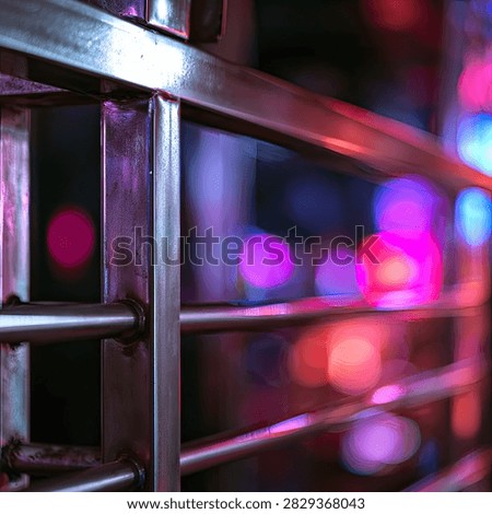 A metallic railing in sharp focus contrasts with a vibrant, blurred background of colorful bokeh lights, creating a sense of urban nightlife.