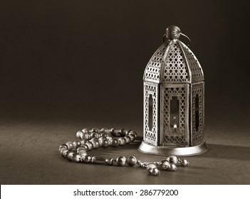 A metallic Ramadan lamp with Islamic rosary beads on black background. Monochromatic image.