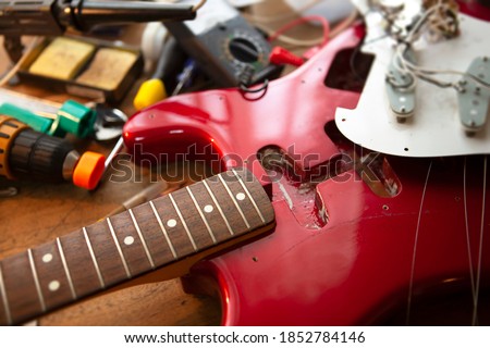 Metallic red electric guitar on guitar repair workbench or a desk,  in repair or maintenance. Pickguard detached. Double cutaway solid body guitar. Shallow depth of field.