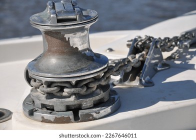 Metallic rusty anchor windlass on a white boat at the sea. Anchor is pulled up with the winch and chain. Metal looks shiny in the sun on a summer day, fun family boat ride. - Powered by Shutterstock
