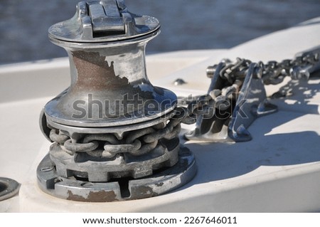 Metallic rusty anchor windlass on a white boat at the sea. Anchor is pulled up with the winch and chain. Metal looks shiny in the sun on a summer day, fun family boat ride.