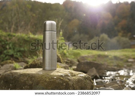 Metallic thermos on stone outdoors, space for text
