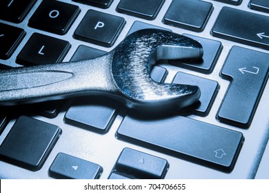 Metallic wrench over a computer keyboard in blue toned, computer and laptop maintenance concept.