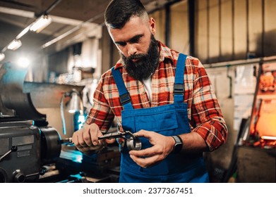 A metallurgist measuring a metal roll cut fitting he created with a caliper. A blue collar worker is standing in a heavy metal industry factory and working with tool while measuring metal parts. - Powered by Shutterstock