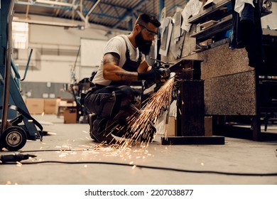 A Metallurgy Worker Kneeling And Cutting Metal Parts With Grinder At Workshop.