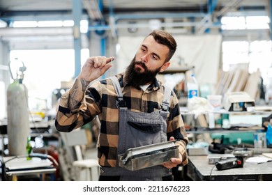 A Metallurgy Worker Looking At Screw In His Hand While Standing In Factory.