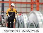 Metalwork manufacturing, warehouse of raw materials. Male factory worker inspecting quality rolls of metal sheet in factory during manufacturing process, wearing safety uniform, use digital tablet