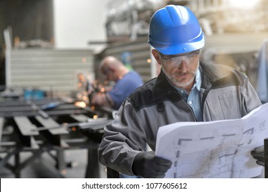 Metalworker in factory reading instructions on blueprint